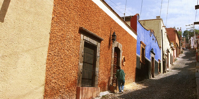 Mexico, San Miguel De Allende, Person Standing In Front Of A Doorway On A Cobblestone Roadway. (Photo by Education Images/UIG via Getty Images)