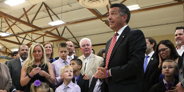 Surrounded by state lawmakers and the families of students who were victims of bullying, Nevada Gov. Brian Sandoval signs an anti-bullying bill into law at Carson Middle School in Carson City, Nev., Wednesday, May 20, 2015. (AP Photo/Cathleen Allison)