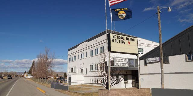 In this Jan. 28, 2015 photo, an American flag and a Montana state flag fly in front of Harrison High School, in Harrison, Mont. Harrison High School in 2013 banned a student after he brought two handguns to school. Now, after that student has served a year in a juvenile facility and received two years of counseling, the child's parents are having a hard time finding a school in the state that will accept their child, now 16, and who they say has changed for the better. (AP Photo/Alison Noon)