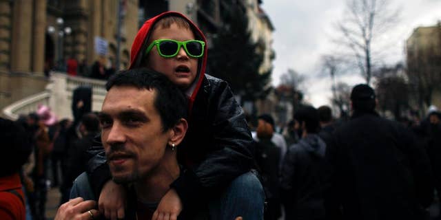 A man carries a boy on his shoulders during a protest in front of the Nikola Tesla Museum in Belgrade, Serbia, Saturday, March 8, 2014. Several hundred people are joining the dispute between the Serbian Orthodox Church and Serbia’s nationalist authorities because of a bid to move the remains of visionary scientist Nikola Tesla from the Tesla Museum to a church in Belgrade. Famed Serbian scientific pioneer in electricity, radio and x-rays, died in 1943. (AP Photo/ Marko Drobnjakovic)