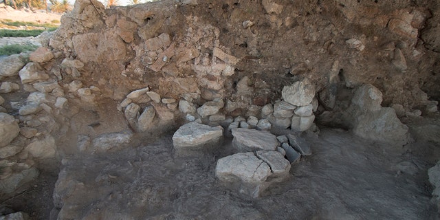 An excavated area at Tel Megiddo from 2014 shows a stone-paved floor that has fire-blackened sediment. The wall consists of collapsed red and yellowish mud bricks.