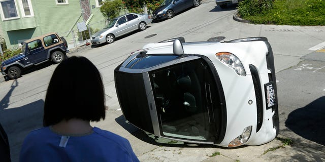 Shelley Gallivan looks toward a tipped over Smart car which belongs to her friend in San Francisco, April 7, 2014.