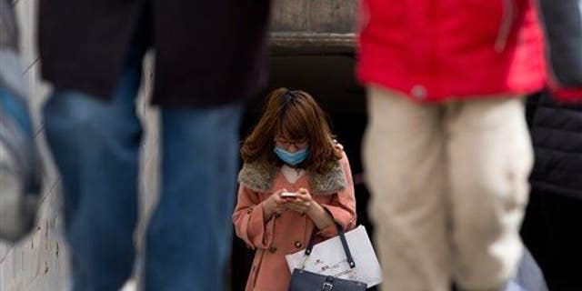 A Chinese woman wears a face mask checking her smartphone in Beijing.