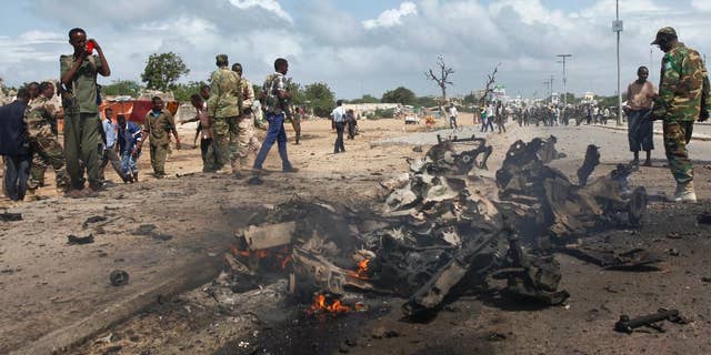 Somali soldiers stand near the wreckage at the scene of a suicide car bomb attack which targeted a convoy of foreign officials, in Mogadishu, Somalia Wednesday, June 24, 2015. (AP Photo)
