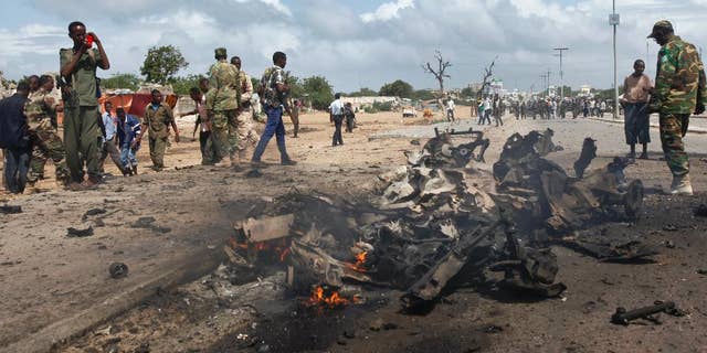 Somali soldiers stand near the wreckage at the scene of a suicide car bomb attack which targeted a convoy of foreign officials, in Mogadishu, Somalia Wednesday, June 24, 2015. (AP Photo)