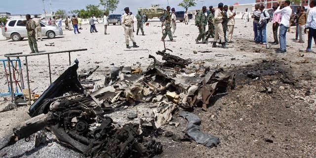Somali soldiers stand near the wreckage of a suicide car bomb near the Somali parliament in Mogadishu, Somalia, Saturday, July 5, 2014. A Somali police officer says troops have thwarted an attack by a suicide bomber outside the heavily guarded parliament headquarters. Capt. Mohamed Hussein, a senior Somali police officer says troops stopped a suicide car bomber who detonated his explosive-laden car at a checkpoint near the entrance to Somalia's parliament. (AP Photo/Farah Abdi Warsameh)