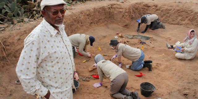 In this photo taken Tuesday, Feb. 18, 2014, Chairman of the Somaliland War Crimes Commission Kadar Ahmed, left, oversees members of the Peruvian Forensic Anthropology Team as they work to uncover bodies buried in a mass grave in Hargeisa, Somaliland, a breakaway region of Somalia. An American volunteer gently brushes away dirt to reveal the bones of a Somali victim buried in a mass grave some 30 years ago. Tens of thousands of skeletons may lie in mass graves here, on the northern edge of Somalia, where many want to see justice prevail, even if delayed. Last year 38 bodies were uncovered in two graves by the Somaliland War Crimes Investigation Commission, which is overseeing the work on a third site where another dozen bodies are buried. (AP Photo/Jason Straziuso)
