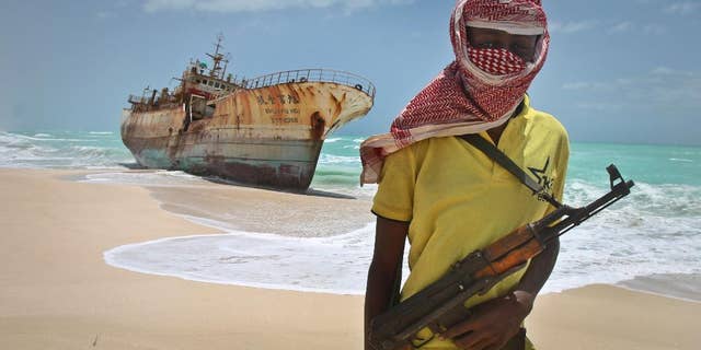 FILE - In this Sunday, Sept. 23, 2012 file photo, masked Somali pirate Hassan stands near a Taiwanese fishing vessel that washed up on shore after the pirates were paid a ransom and released the crew, in the once-bustling pirate den of Hobyo, Somalia. A U.N. official said Friday, Feb. 27, 2015 that Somali pirates have released four Thai sailors who were held hostage for nearly five years, after their ship the FV Prantalay 12 was seized by Somali pirates on April 18, 2010. (AP Photo/Farah Abdi Warsameh, File)