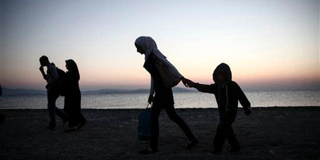 People walk along a beach on the Greek southeastern island of Kos, Wednesday, Aug. 12, 2015.