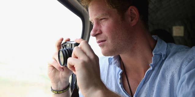 FILE - In this Dec 8, 2014, file photo, Prince Harry takes a photograph out of the window of a helicopter as he travels over the Muluti Mountains on his way to visit a herd boy night school constructed by his Sentebale charity, in Mokhotlong, Lesotho. Prince Harry has been on a private visit to Kruger National Park, South Africa's flagship wildlife park, where poachers have killed rhinos in record numbers and clashed with rangers, the service said in a statement emailed Thursday, Aug. 13, 2015, to The Associated Press. (Chris Jackson/Pool Photo via AP, File)