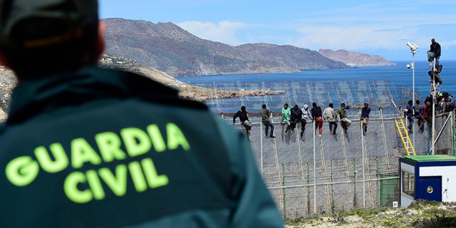 MELILLA, SPAIN - APRIL 03: A Guardia Civil Police Officer watches African migrants who attemped to scale the fence at the border between Morocco and the North African Spanish enclave of Melilla, on April 3, 2014, in Melilla, Spain. Roughly 70 sub-Saharan migrants tried climb the fence into Melilla this morning, one had to be treated by paramedics. Melilla is a Spanish city and an exclave on the north coast of Africa sharing a border with Morocco. Almost one week ago Some 800 sub- Saharan people made several attempts to reach Spain and according to official sources, ten of them managed to enter Spanish territory. (Photo by Alexander Koerner/Getty Images)