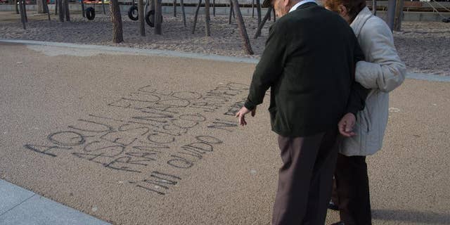A couple stop to look at words painted on the ground by the Manzanarez river near where a 43-year-old Deportivo fan was killed, Madrid, Spain, Monday, Dec. 1, 2014. The man died and 11 others suffered minor injuries after a fight broke out across the river from Atletico de Madrid's soccer stadium between its fans and those of visiting team Deportivo La Coruna on Sunday. Madrid's Clinico San Carlos hospital said a man died of injuries sustained in the clash between rival fans that broke out hours before the game near the Vicente Calderon stadium and had to be removed from the river. Police made several arrests. Writing in Spanish reads: 'Here, Francisco J. Romero was murdered. I will never forget or Forgive' (AP Photo/Paul White)