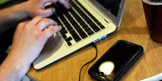 ** FOR USE MONDAY, DEC. 28 AND THEREAFTER ** FILE - In this May 13, 2009, file photo, Jonathan Hutcheson works on his laptop as his iPhone lays beside it at a coffee shop in Columbia, Mo. Wireless phone companies fear they're in danger of running out of room within the spectrum of wireless frequencies, so they want the government to give them bigger slices of airwaves _ even if other users have to give up rights to theirs. (AP Photo/L.G. Patterson, File)