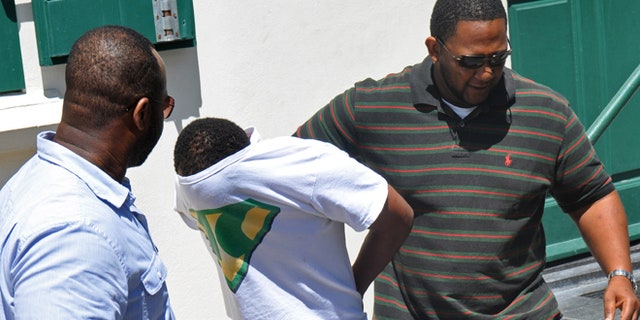 With his T-shirt pulled over his head, Jamaican Meyshane Johnson, center, a suspect in the slaying of a South Carolina couple, is escorted by police officers outside the court building after his arraignment in Philipsburg, St. Maarten.