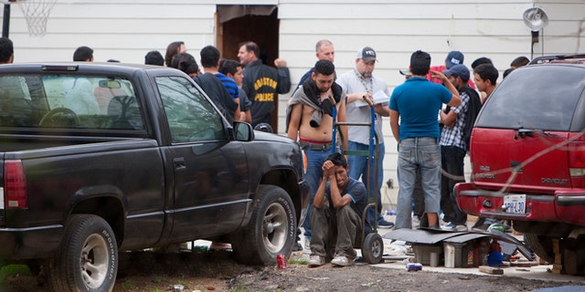 People wait outside a house, Wednesday, March 19, 2014, in southeast Houston. A house overflowing with more than 100 people presumed to be in the United States illegally was uncovered just outside Houston on Wednesday, a police spokesman said. The suspected stash house was found during a search for a 24-year-old woman and her two children that were reported missing by relatives Tuesday after a man failed to meet them, said a spokesman for the Houston Police Department. (AP Photo/Houston Chronicle, Cody Duty)