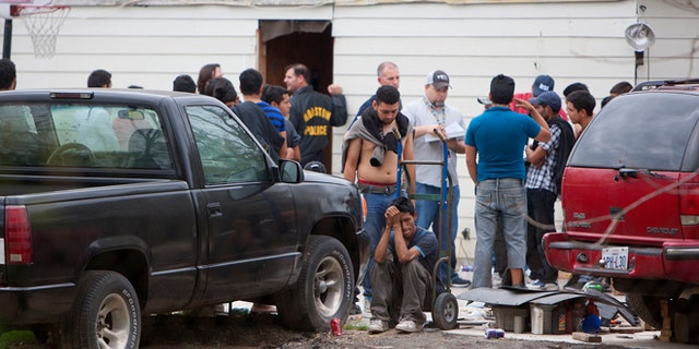 People wait outside a house, Wednesday, March 19, 2014, in southeast Houston. A house overflowing with more than 100 people presumed to be in the United States illegally was uncovered just outside Houston on Wednesday, a police spokesman said. The suspected stash house was found during a search for a 24-year-old woman and her two children that were reported missing by relatives Tuesday after a man failed to meet them, said a spokesman for the Houston Police Department. (AP Photo/Houston Chronicle, Cody Duty)