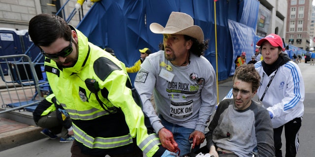 FILE - In this April 15, 2013 file photo, an emergency responder and volunteers, including Carlos Arredondo in the cowboy hat, push Jeff Bauman in a wheel chair after he was injured in an explosion near the finish line of the Boston Marathon Monday, April 15, 2013 in Boston.   Arredondo and Bauman are among the guests who will sit with first lady Michelle Obama Tuesday when President Barack Obama delivers the annual State of the Union address.   (AP Photo/Charles Krupa, File)