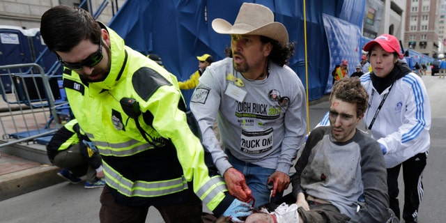 FILE - In this April 15, 2013 file photo, an emergency responder and volunteers, including Carlos Arredondo in the cowboy hat, push Jeff Bauman in a wheel chair after he was injured in an explosion near the finish line of the Boston Marathon Monday, April 15, 2013 in Boston. Arredondo and Bauman are among the guests who will sit with first lady Michelle Obama Tuesday when President Barack Obama delivers the annual State of the Union address. (AP Photo/Charles Krupa, File)