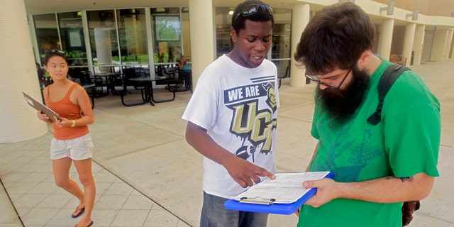 FILE: July 31, 2012: Aubrey Marks, left, watches Jordan Allen, center, as he helps student Casey Eirhstaedt, right, register to vote at the University of Central Florida in Orlando, Fla.