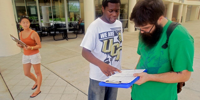 FILE: July 31, 2012: Aubrey Marks, left, watches Jordan Allen, center, as he helps student Casey Eirhstaedt, right, register to vote at the University of Central Florida in Orlando, Fla.