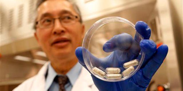 Dr. Thomas Louie, an infectious disease specialist, holds a container of stool pills in triple-coated gel capsules in his lab in Calgary, Alberta, Canada on Thursday, Sept. 26, 2013.