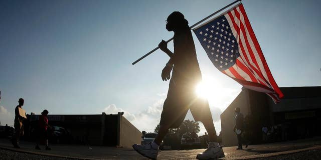 FILE - In this Aug. 18, 2014 file photo, Duane Merrells walks with an upside down American flag during a protest for Michael Brown in Ferguson, Mo. Ferguson officials were inundated with thousands of open-records requests from media outlets and the public following the shooting. In response, the St. Louis suburb sought payments of thousands of dollars before they would even begin to fulfill some of those requests, a decision defended by Ferguson’s city attorney. The Missouri attorney general's office received several complaints from media outlets, including The Associated Press, that Ferguson was charging excessive fees. (AP Photo/Charlie Riedel, File)