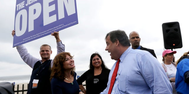 New Jersey Gov. Chris Christie, right, talks to Carla Pilla, of Seaside Heights, N.J., while Robert Hilton, left, executive director of the Jersey Shore Convention and Visitor's Bureau, holds a sign, Friday, May 24, 2013, in Seaside Heights, N.J. Christie cut a ribbon to symbolically reopen the state's shore for the summer season, seven months after being devastated by Superstorm Sandy. Several beach communities have annual beach ribbon cuttings, announcing they are back in business. But this year's ceremonies are more poignant seven months after a storm that did an estimated $37 billion of damage in the state. (AP Photo/Julio Cortez)