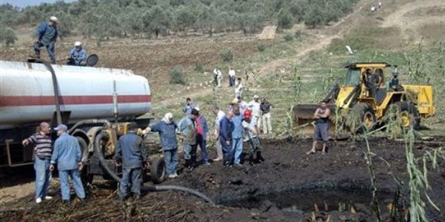 July 29, 2011: In this photo released by the Syrian official news agency SANA, workers pump oil from the site of a bomb blast that struck a major oil pipeline in the western town of Talkalakh, Syria.