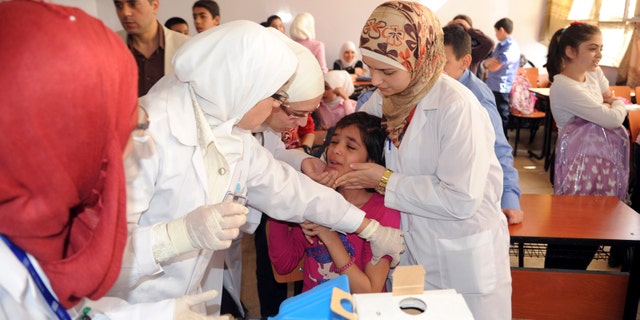 Syrian health workers administer polio vaccination to a girl at a school in Damascus, in this file photo taken by Syria's national news agency SANA on October 20, 2013.