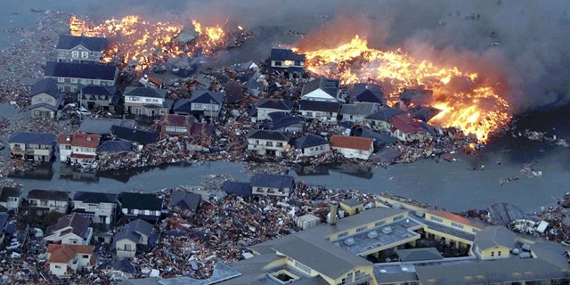 March 11: Houses are in flame while the Natori river is flooded over the surrounding area by tsunami tidal waves in Natori city, Miyagi Prefecture.