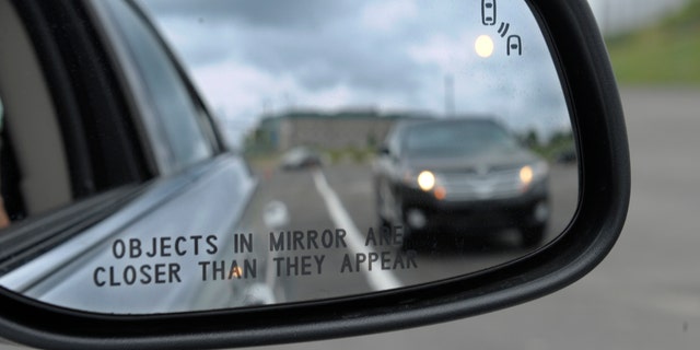 This May 22, 2012 file photo shows a side mirror warning signal in a Ford Taurus at an automobile testing area in Oxon Hill, Md. Federal officials are planning to announce Monday whether automakers should be required to equip new cars and light trucks with technology that enables vehicles to communicate with each other to prevent collisions. Such vehicle-to-vehicle communication could eventually transform traffic safety.