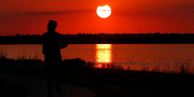 A jogger runs in front of the sun near the end of a partial solar eclipse at Lake Hefner in Oklahoma City, Thursday, Oct. 23, 2014.