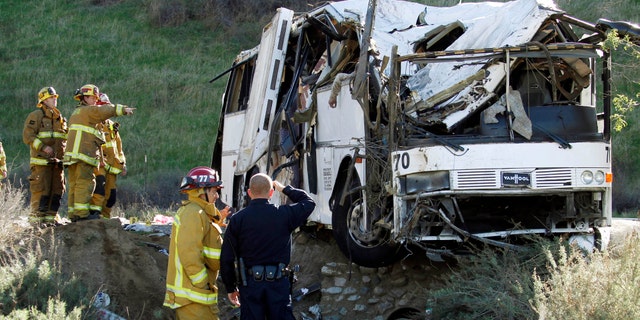 EDITORS NOTE GRAPHIC CONTENT - Firefighters and a California Highway Patrol officer survey the scene of an accident where at least eight people were killed and 38 people were injured after a tour bus, left, carrying a group from Tijuana, Mexico crashed with two other vehicles just north of Yucaipa, Calif., Sunday, Feb. 3, 2013. The arm of a deceased victim is seen at top center. (AP Photo/Reed Saxon)