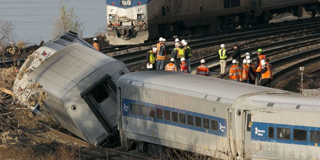 FILE - In this Dec. 1, 2013 file photo, an Amtrak train, top, traveling on an unaffected track, passes a derailed Metro North commuter train in the Bronx borough of New York. (AP Photo)