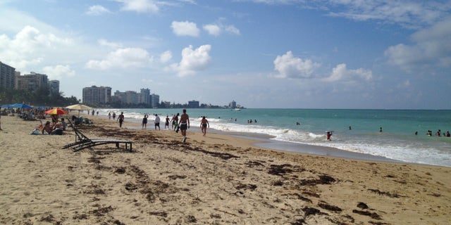In this Oct. 2014 photo, beachgoers enjoy the sun and sand at Isla Verde Beach in San Juan, Puerto Rico. Puerto Rico, a U.S. territory, offers all the comforts of domestic travel - easy entry, no extra charges for cell phone service, and the U.S. dollar as the currency - along with Caribbean beaches and Latin culture, waterfalls, colonial Spanish history and good food and drink. (AP Photo/Kristi Eaton)