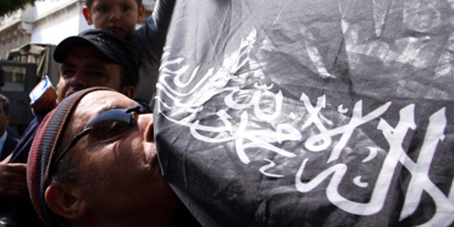 April 19, 2012: A Salafi Muslim kisses a flag reading "Only one god and Mohammed is his Prophet" ; outside the courthouse in Tunis for the trial of the Tunisian TV station for airing the prize-winning animated feature "Persepolis"; and allegedly insulted Islam.