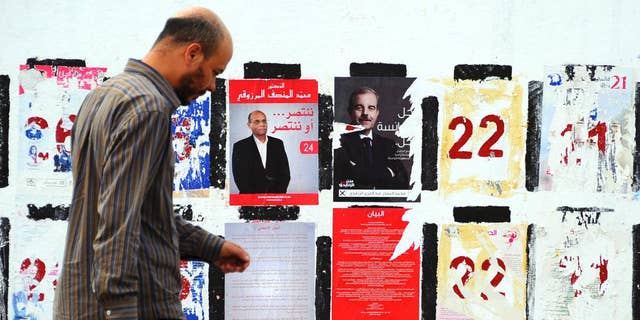 In this photo taken Wednesday, Nov. 5, 2014, a man walks past electoral posters for the upcoming presidential elections in Tunis. Campaign posters and banners for next week’s presidential elections have covered the walls of Tunisia’s cities and towns, papering over the flaking posters from the parliamentary elections just three weeks ago. (AP Photo/Hassene Dridi)