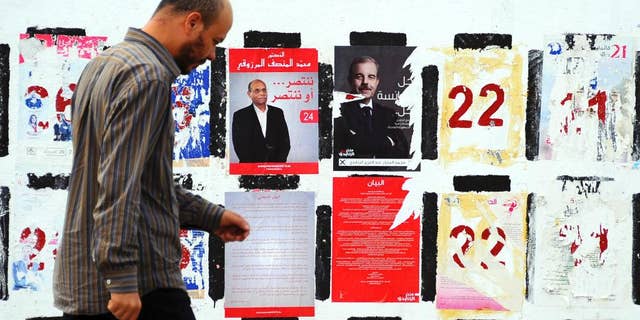 In this photo taken Wednesday, Nov. 5, 2014, a man walks past electoral posters for the upcoming presidential elections in Tunis. Campaign posters and banners for next week’s presidential elections have covered the walls of Tunisia’s cities and towns, papering over the flaking posters from the parliamentary elections just three weeks ago. (AP Photo/Hassene Dridi)