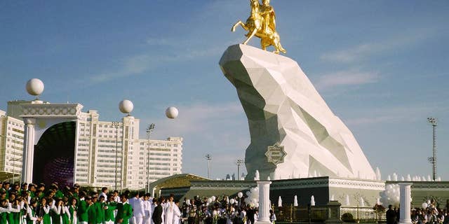 Ljudi se okupljaju na ceremoniji otkrivanja spomenika u Ashgabatu, Turkmenistan, ponedjeljak, 25. svibnja 2015. Izolirana energetski bogata srednjoazijska država Turkmenistan otkrila je statuu predsjednika sa zlatnim lišćem u gesti s namjerom da ugasi rastući kult ličnosti čelnika . Spomenik od 21 metra koji je javnosti predstavljen u ponedjeljak sastoji se od kipa predsjednika Gurbangulyja Berdymukhamedova na vrhu konja postavljenog na visoku hrpu mramora. (AP Photo/Alexander Vershinin)