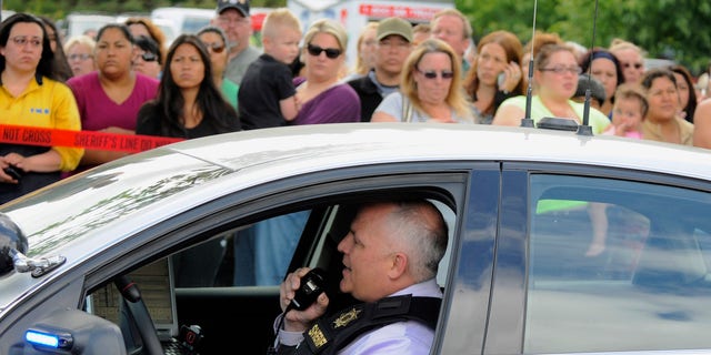 In this June 10, 2014, file photo, a sheriff's deputy talks on his radio as parents wait to be reunited with their children at a shopping center parking lot in Wood Village, Ore., after a shooting at Reynolds High School in Troutdale, Ore.