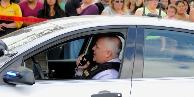 In this June 10, 2014, file photo, a sheriff's deputy talks on his radio as parents wait to be reunited with their children at a shopping center parking lot in Wood Village, Ore., after a shooting at Reynolds High School in Troutdale, Ore.