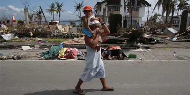 A man, holding a boy, walks past dead bodies along the streets in typhoon-ravaged Tacloban city, Leyte province central Philippines on Monday, Nov. 11, 2013. Typhoon-ravaged Philippine islands faced an unimaginably huge relief effort that had barely begun Monday, as bloated bodies lay uncollected and uncounted in the streets and survivors pleaded for food, water and medicine. (AP Photo/Aaron Favila)