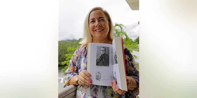 In this Sept. 10, 2015 photo, Frances Serantes Gomez poses with a photo of her great uncle, Archbishop Enrique Perez Serantes, at her home in Coral Gables, Florida. Serantes Gomez's great uncle is the former archbishop of Santiago, Cuba who saved Fidel Castro’s life. After Castro seized power, Serantes’ support turned to opposition and the prelate’s family fled. Frances is among several hundred Cuban-Americans expected to make a pilgrimage to Cuba for Pope Francis’ visit, and among thousands who are trying to finally put five decades of bitterness behind them. (AP Photo/Alan Diaz)