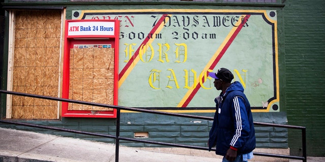 FILE - In this April 30, 2015 file photo, a man walks past the damaged Oxford Tavern in Baltimore. In a presidential campaign where candidates are jockeying to be champions of the middle class and courting donations from the wealthy, the poor are inching their way into the debate. Tensions in Baltimore, Ferguson, Missouri, and elsewhere have sparked examinations of the relationship between poor communities and the police, as well as the systemic problems that have trapped many of the 45 million Americans living in poverty. But addressing the economic, education, and security issues that have plagued underprivileged neighborhoods for decades remains a politically elusive challenge. (AP Photo/David Goldman, File)