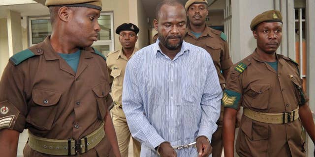 FILE - In this Friday, May 22, 2015 file photo, rebel leader of the Ugandan Allied Democratic Forces (ADF), Jamil Mukulu, center, is escorted by prison wardens as he appears at a magistrates court to challenge extradition proceedings against him, in Dar es Salaam, Tanzania. The head of Interpol in Uganda said Friday, July 10, 2015, that Mukulu, a most-wanted Ugandan extremist who is accused of committing atrocities in Uganda and Congo, has been extradited to Uganda. (AP Photo/Khalfan Said, File)