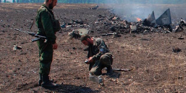 In this framegrab made from a video provided by press service of the rebel Donetsk People's Republic and icorpus.ru,  pro-Russians collect parts of the burning debris of a Ukrainian military fighter jet, shot down at Savur Mogila, eastern Ukraine, Wednesday, July 23, 2014. Two Ukrainian military Sukhoi-25 fighters have been shot down in the east, according to the country's Defense Ministry. (AP Photo/icorpus.ru, Press Service of the rebel Donetsk People's Republic)