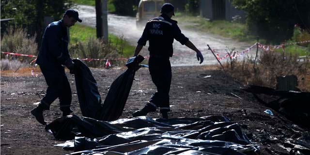 July 21, 2014: Ukrainian Emergency workers carry a victim's body in a plastic bag as other bodies are laid on the ground nearby at the crash site of Malaysia Airlines Flight 17 near the village of Hrabove. (AP Photo/Dmitry Lovetsky)