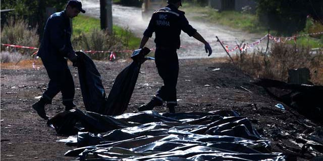 July 21, 2014: Ukrainian Emergency workers carry a victim's body in a plastic bag as other bodies are laid on the ground nearby at the crash site of Malaysia Airlines Flight 17 near the village of Hrabove. (AP Photo/Dmitry Lovetsky)