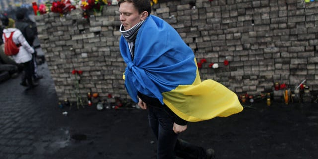 February 23, 2014: A youth draped in Ukraine's flag passes by a memorial to protesters killed in clashes with the police at Independence Square in Kiev, Ukraine. (AP Photo/ Marko Drobnjakovic)