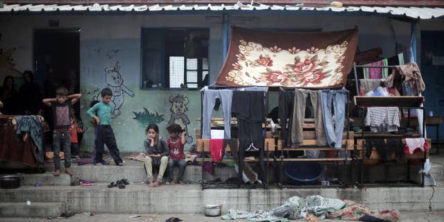 FILE - In a July 28, 2014 file photo, Palestinian children sit next to hanged clothes, on the First day of Eid al-Fitr in a United Nations school where dozens of families have sought refuge after fleeing their homes in fear of Israeli airstrikes, in the Jabaliya refugee camp, northern Gaza Strip. A U.N. inquiry has found that at least 44 Palestinians were killed and at least 227 injured by "Israeli actions" while sheltering at U.N. locations during last year's Gaza war. Secretary Ban Ki-moon said Monday, April 27, 2015, he deplores the deaths and calls U.N. locations "inviolable."(AP Photo/Khalil Hamra, File)